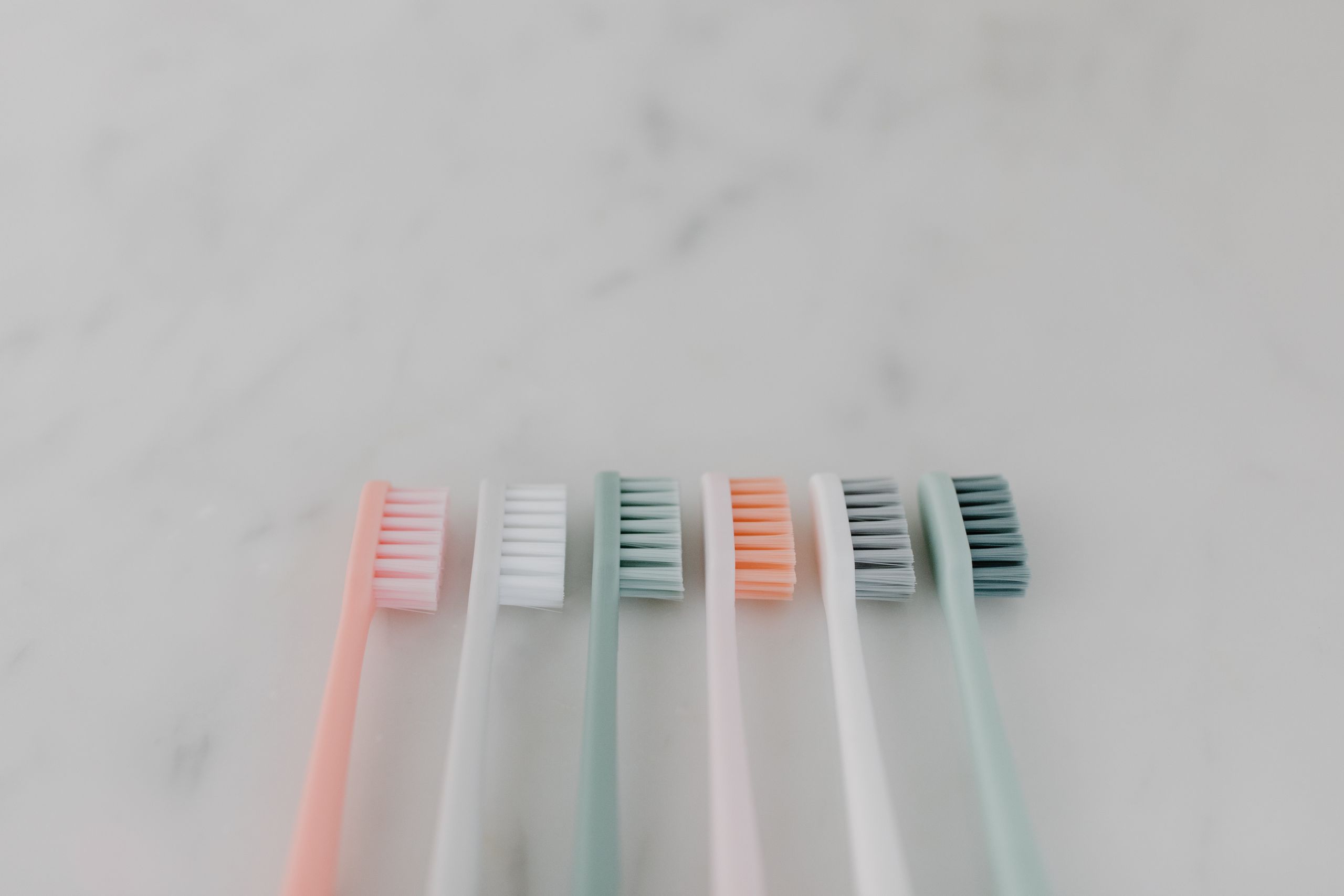 A row of colorful pastel toothbrushes aligned on a smooth marble surface.
